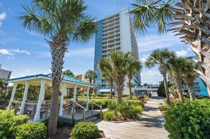 Ein Resort mit einem Kiosk, Palmen, einer Holzpromenade und einem hohen Gebäude im Hintergrund.