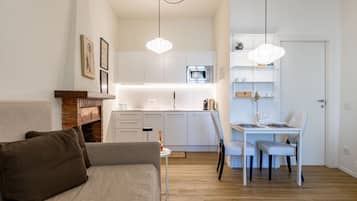 Un soggiorno moderno con un divano, un tavolo da pranzo con sedie, un angolo cottura con pensili e un forno a microonde, e lampade a sospensione.