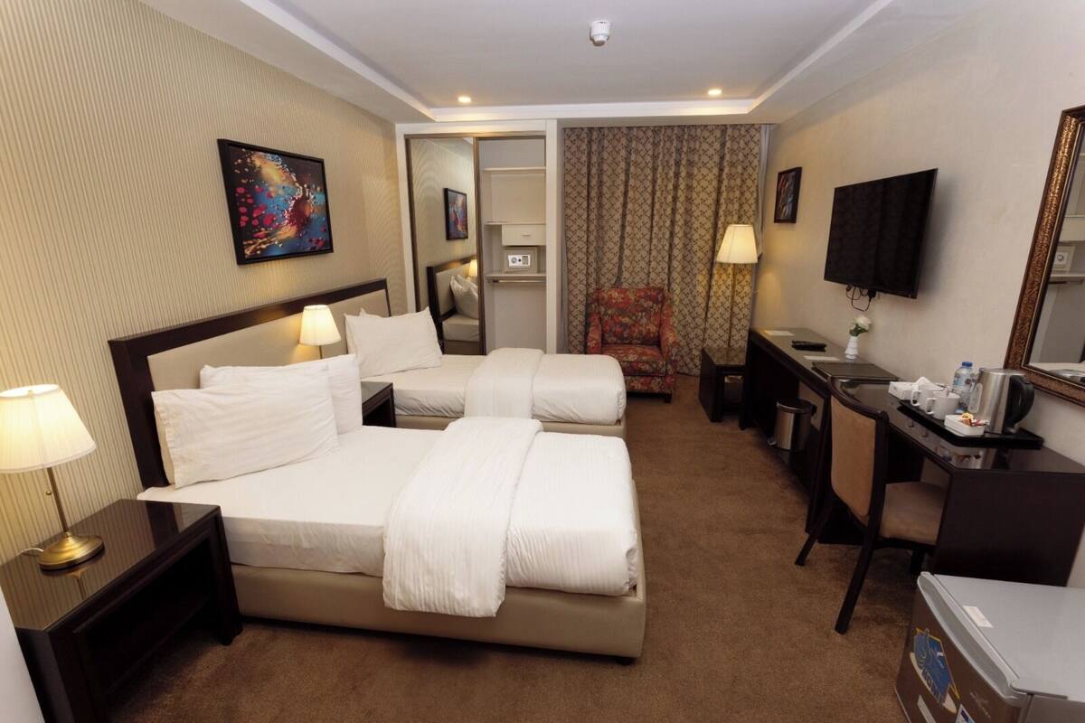 A hotel room with two beds, a desk, a chair, a television, and a bathroom.