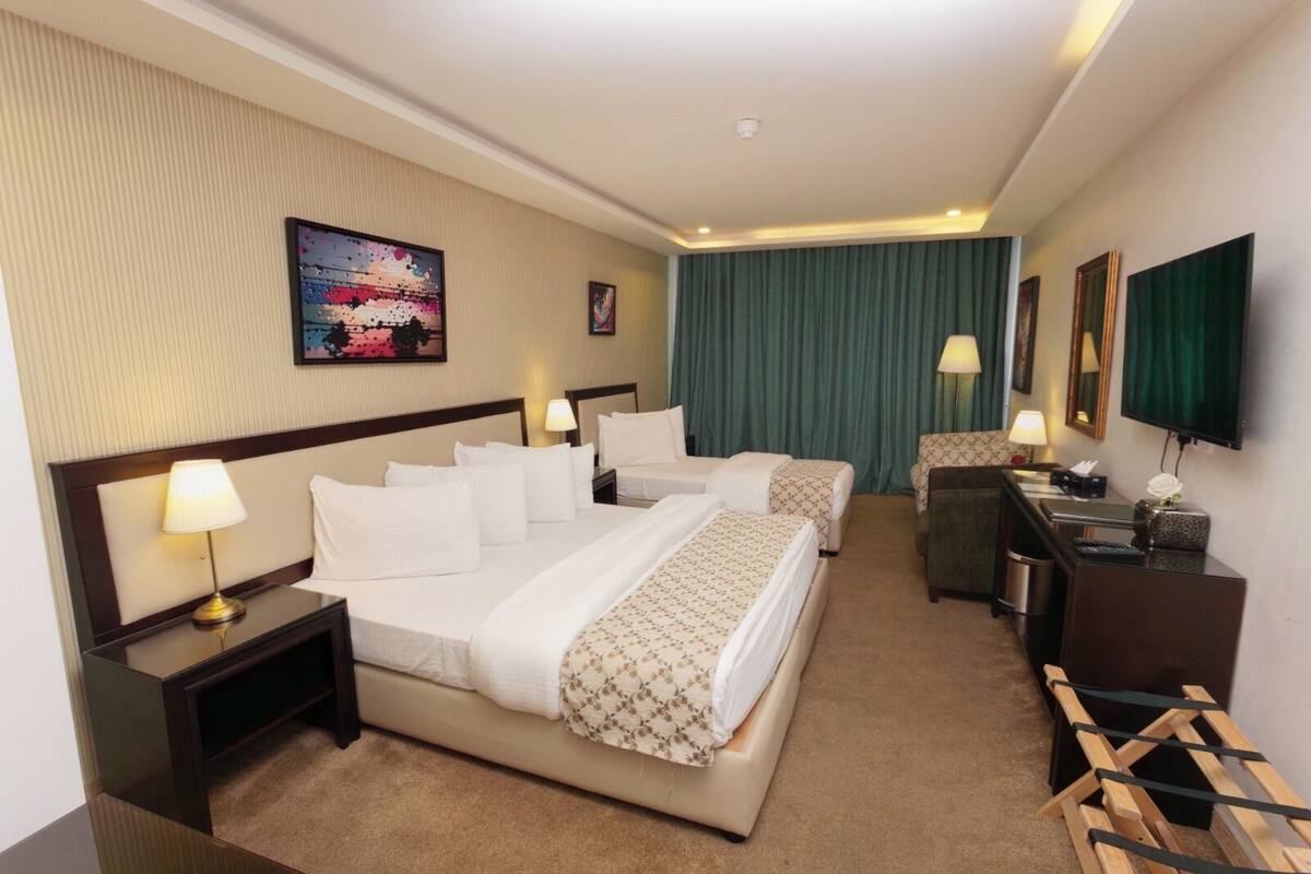 A hotel room with two beds, a desk, a chair, a TV, and a painting on the wall.