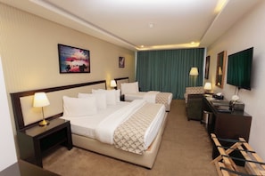 A hotel room with two beds, a desk, a chair, a TV, and a painting on the wall. - Strand Hotel (Amman)