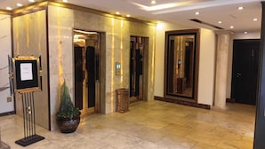 Un vestíbulo de hotel con suelo de mármol, un mostrador de recepción, una planta en maceta y un espejo grande.