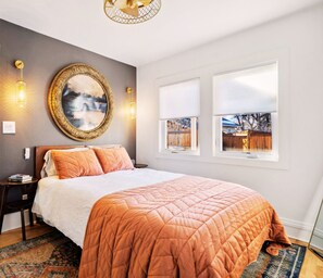 Ein Schlafzimmer mit einem großen Bett, einem runden Spiegel, zwei Fenstern und Blick ins Freie.