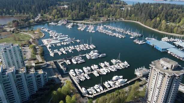 Une vue aérienne d’une marina où sont amarrés de nombreux bateaux, entourée de bâtiments résidentiels et d’une zone boisée.