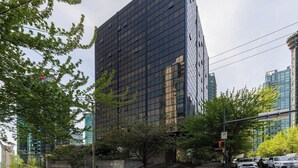Un immeuble moderne de grande hauteur, doté d’une façade en verre, entouré d’arbres et d’autres bâtiments.