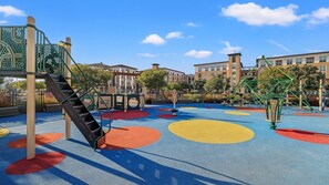 A playground with colorful circular patterns on the ground, a climbing structure, and a swing set.
