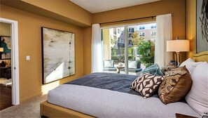 A hotel room with a bed, a large window, and a view of buildings outside.