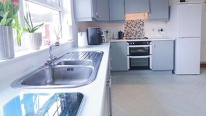 Eine moderne Küche mit grauen Schränken, einer Edelstahl-Spüle, einem Einbauofen und einem weißen Kühlschrank.