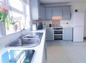 A modern kitchen with grey cabinets, a stainless steel sink, a built-in oven, and a white refrigerator. - 3 Bedroom Pet free Family Holiday Home in Portrush, (Portrush)
