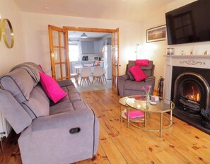 A living room with a sofa, armchair, and a fireplace. There is a dining area in the background. - 3 Bedroom Pet free Family Holiday Home in Portrush, (Portrush)