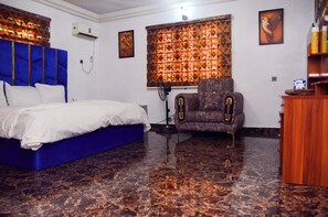 A room with a bed, a chair, a desk, and a window with patterned curtains. - Contemporary Apartment with a distinct African flare (Ibadan)