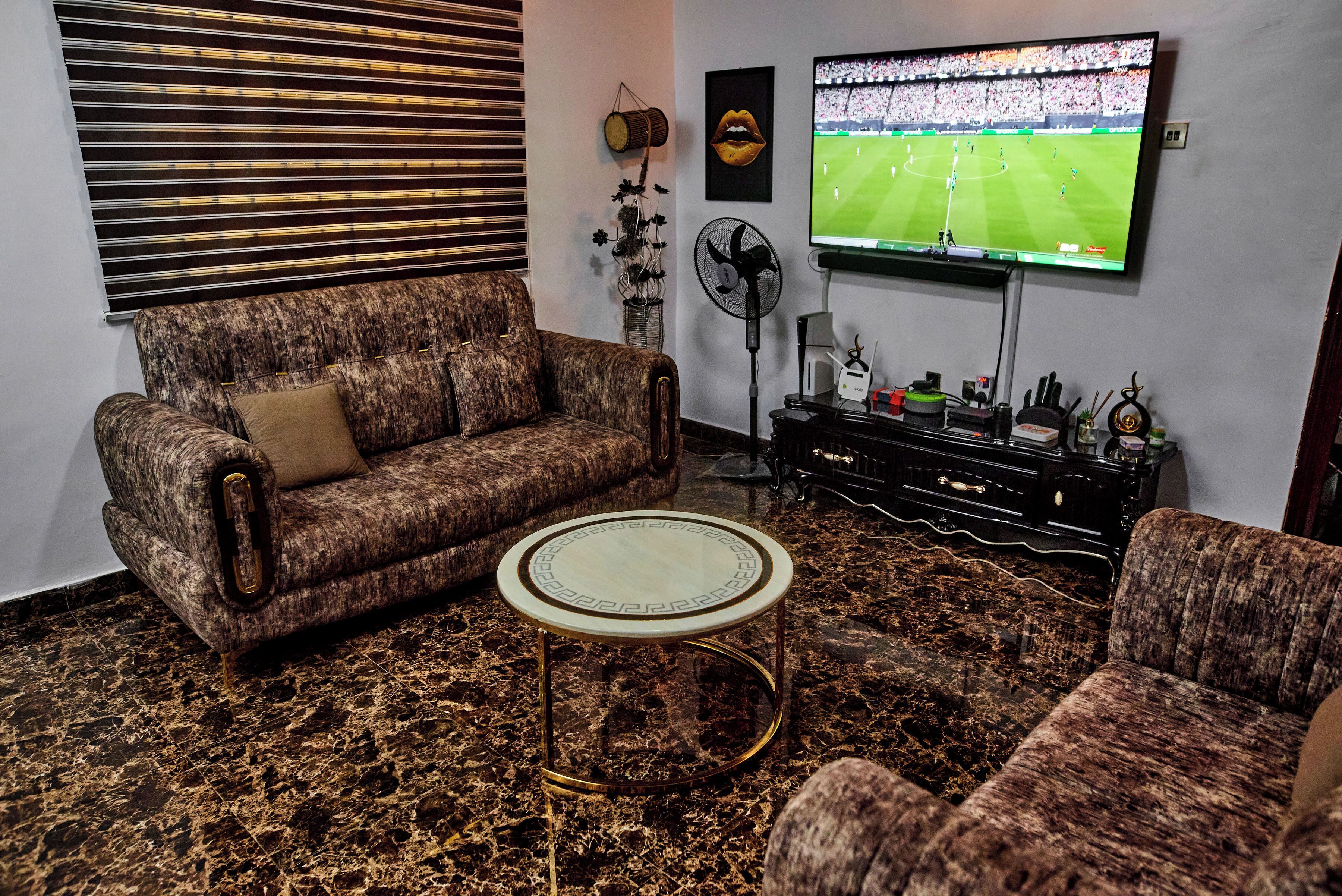 Un soggiorno con un divano decorato, un tavolino rotondo, una TV a parete e una ventaglio decorativo.