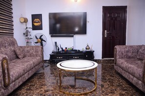 A living room with two sofas, a round coffee table, a TV, a fan, and a door. - Contemporary Apartment with a distinct African flare (Ibadan)