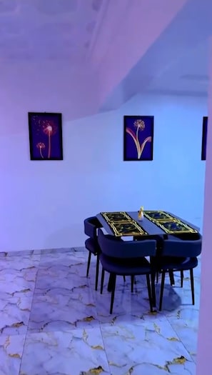 A dining area with a table and chairs, framed artwork on the wall, and a marble floor. - Contemporary Apartment with a distinct African flare (Ibadan)