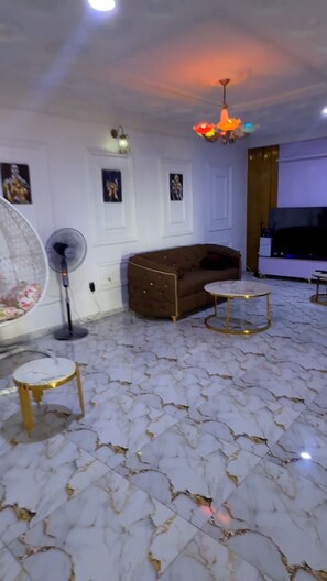 Une pièce comprenant un canapé, une petite table ronde, un ventilateur sur pied et un luminaire fixé au plafond.