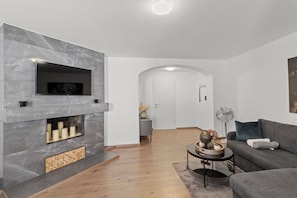 Un salon moderne avec une cheminée, un canapé, une table basse et un téléviseur fixé au mur.
