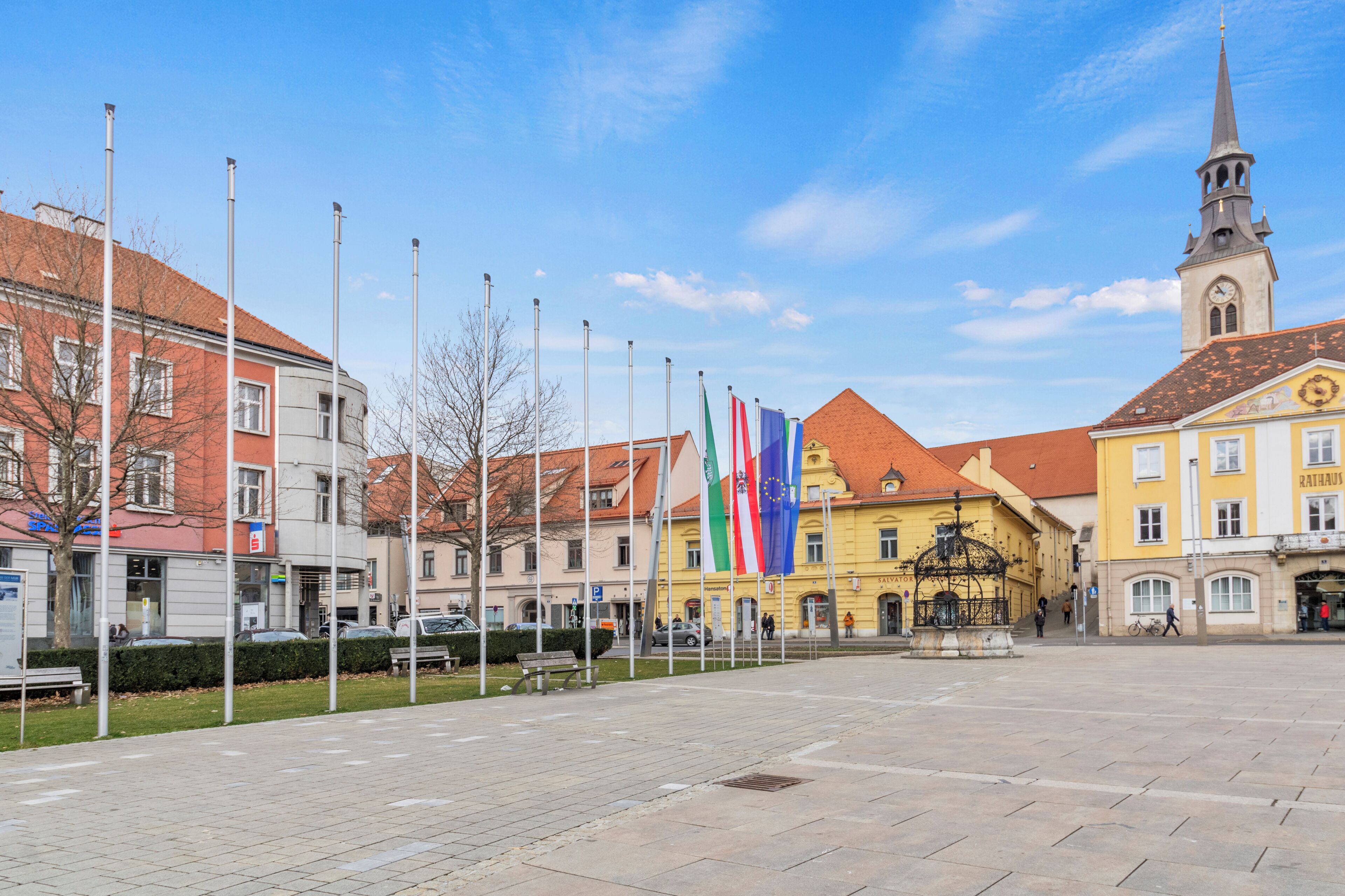 A public square with a fountain, flags, and historic buildings.