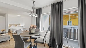 A modern hotel room with a dining area, a bed with white linens, a large window with curtains, and a balcony with a railing. - Faraway Homes Studios Bruck 13 (Bruck an der Mur)