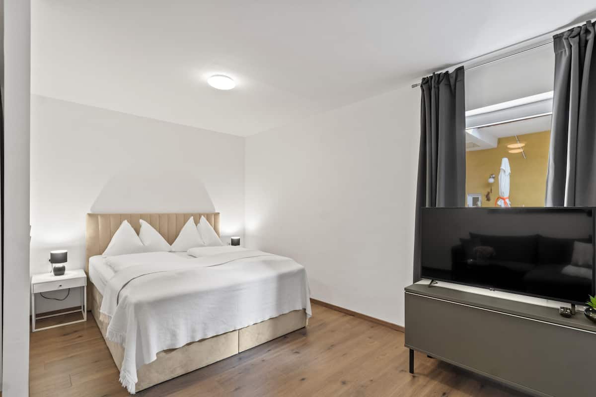 A hotel room with a bed, bedside table, lamp, TV, and a mirror.