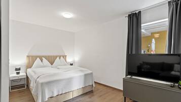 Una habitación de hotel con cama, mesita de noche, lámpara, televisor y espejo.