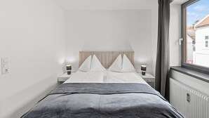 A modern bedroom with a bed, bedside tables, a window, and a radiator. - Faraway Homes Studios Bruck 13 (Bruck an der Mur)