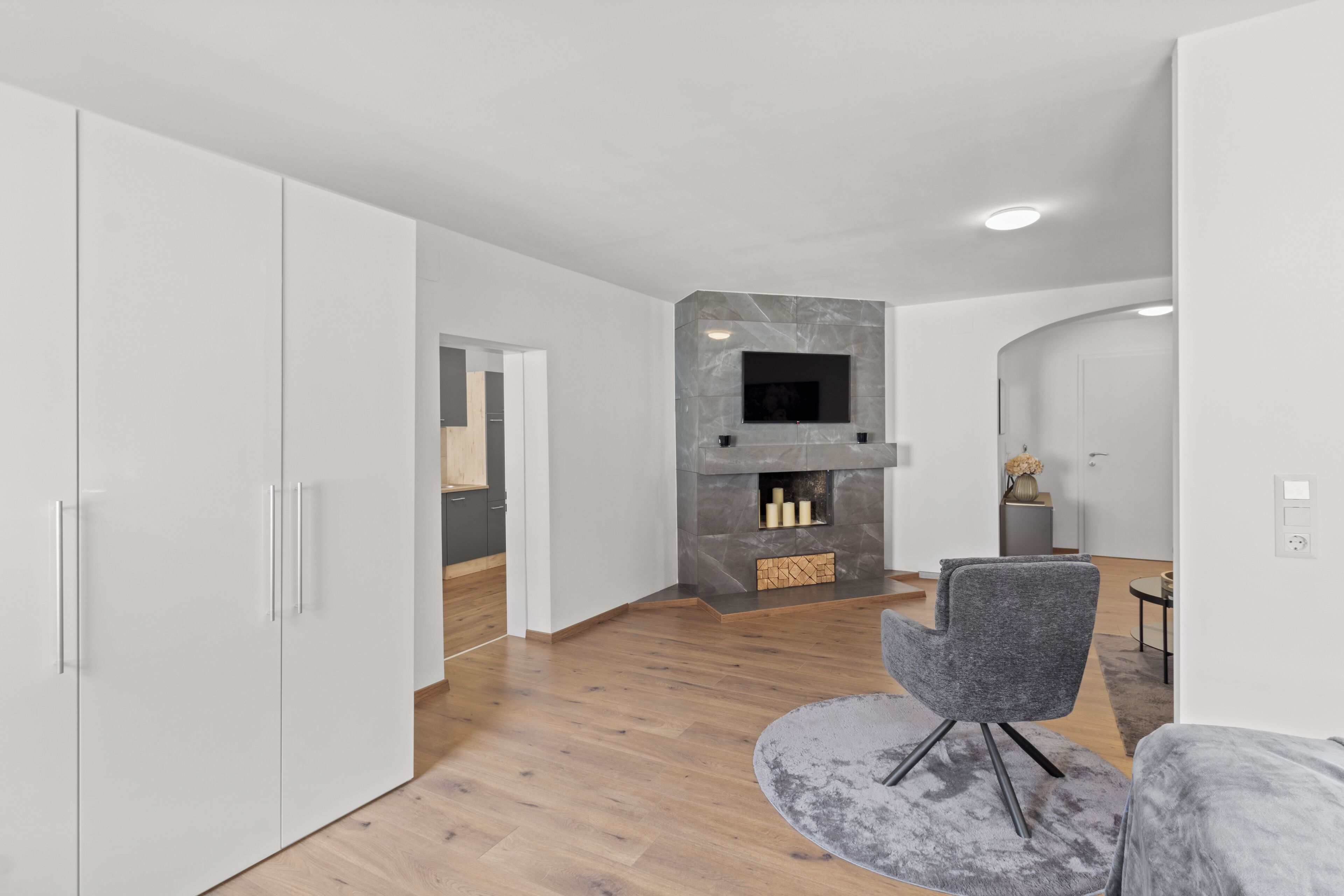A modern living room with a fireplace, a grey armchair, and white cabinets.