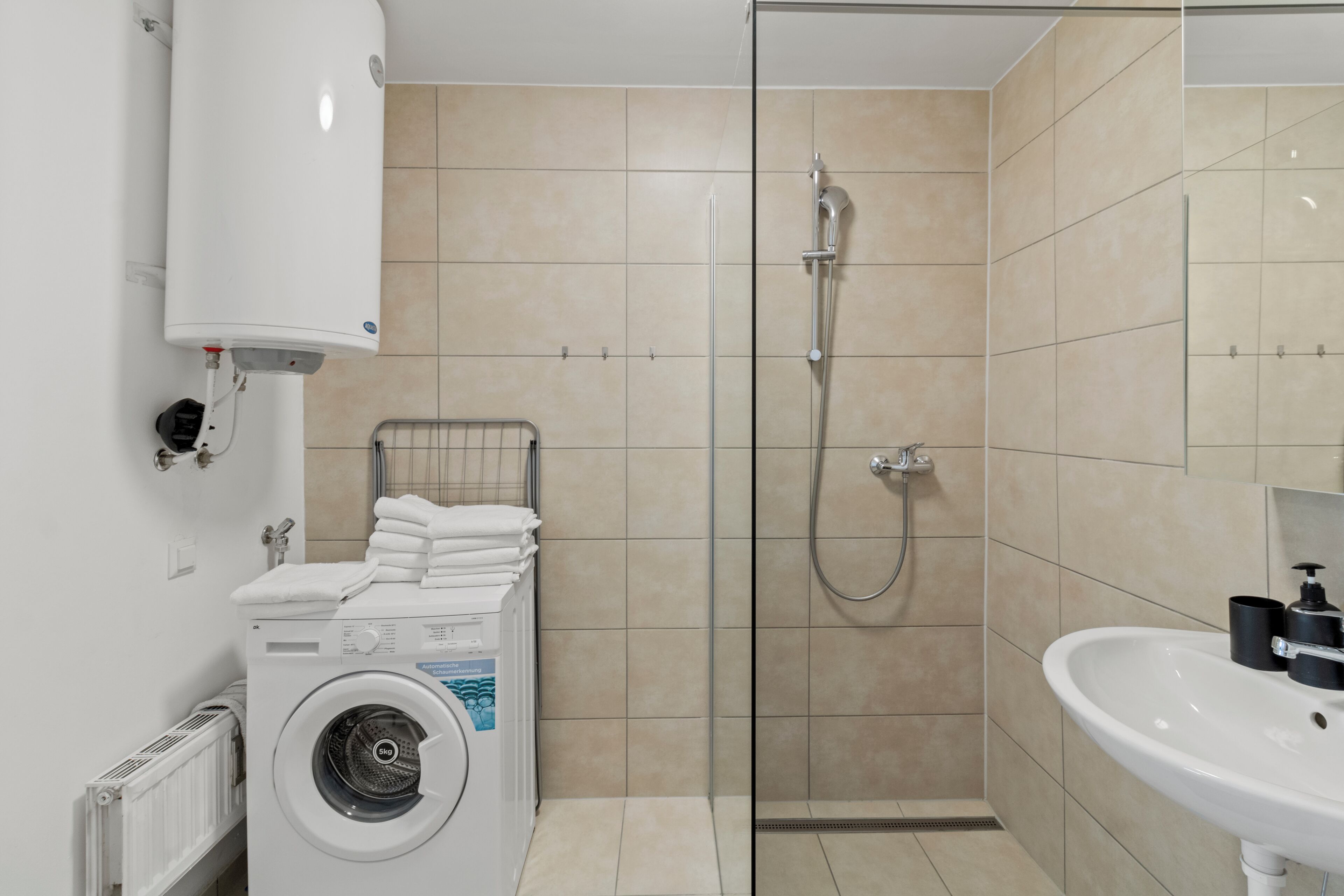 A modern bathroom with a washing machine, a glass-enclosed shower, and a sink.