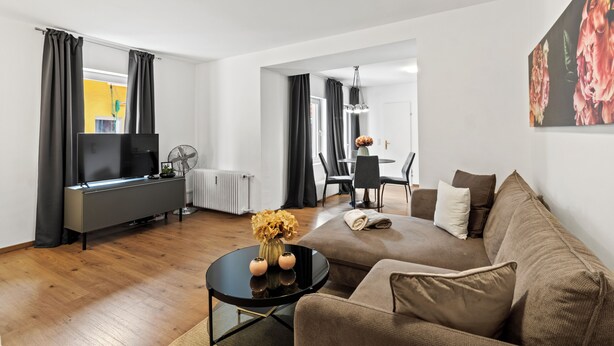 A modern living room with a sofa, coffee table, TV, and a dining area with chairs and a table. - Faraway Homes Studios Bruck 13 (Bruck an der Mur)