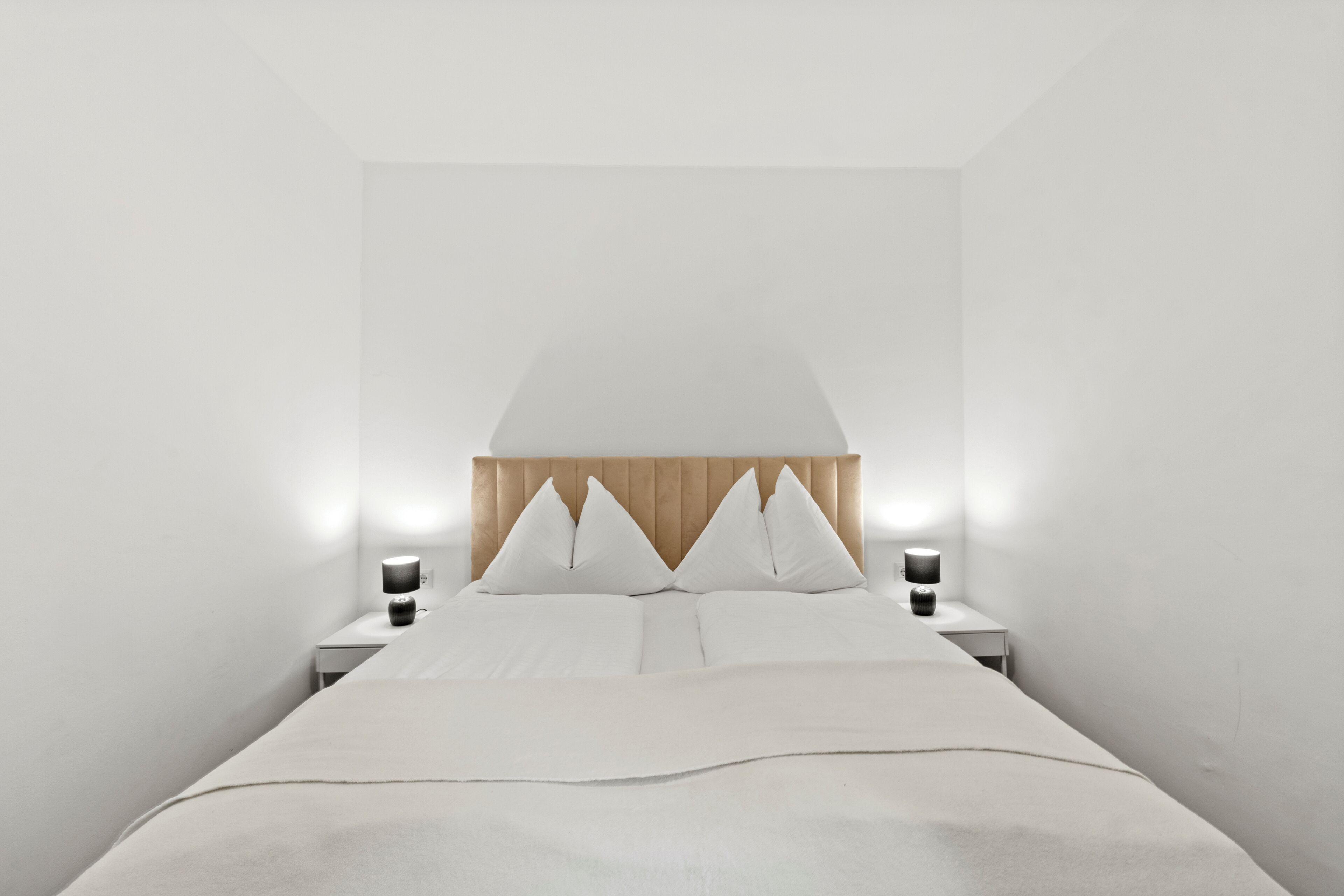 Une chambre à coucher au style minimaliste, avec un lit, deux tables de chevet et une lampe fixée au mur.