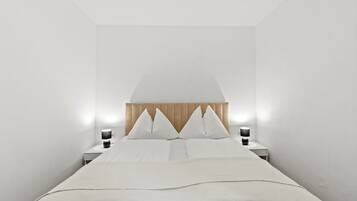 A minimalist bedroom with a bed, two bedside tables, and a wall-mounted lamp.