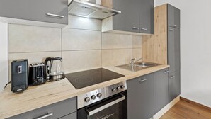 A modern kitchen with grey cabinets, a wooden countertop, a built-in stove, a coffee maker, and a sink. - Faraway Homes Studios Bruck 13 (Bruck an der Mur)