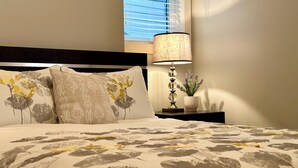 Et soveværelse med seng, puder, et natbord, en lampe og et vindue.