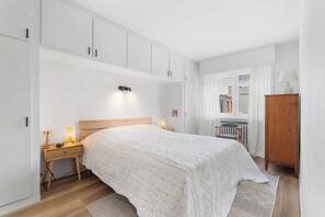 Ein Schlafzimmer mit einem Bett, Nachttischlampen, einem Holznachttisch, einem Holzschrank und einer Heizung.