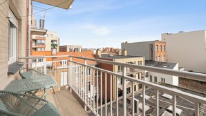 Ein Balkon mit einem Metalltisch und Stühlen, mit Blick auf eine Stadtlandschaft mit verschiedenen Gebäuden und blauem Himmel.