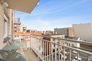 Ein Balkon mit einem Metalltisch und Stühlen, mit Blick auf eine Stadtlandschaft mit verschiedenen Gebäuden und blauem Himmel.