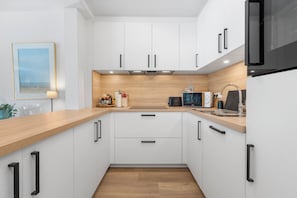 Eine moderne Küche mit weißen Schränken, einer Holz Arbeitsplatte und einer schwarzen Mikrowelle.