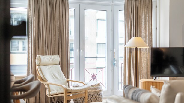 Ein Wohnzimmer mit einer Couch, einem Schaukelstuhl, einem Fernseher und einem Balkon mit Vorhängen.