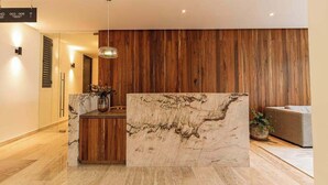 A reception desk with a marble top, wooden paneling on the wall, and a hanging pendant light. - Ceiba 25 | Rooftop Pool, Gym & 5th Ave Condo (Playa del Carmen)