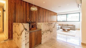 A modern reception area with a marble counter, wooden paneling, a hanging pendant light, and a seating area with a sofa and coffee table. - Ceiba 25 | Rooftop Pool, Gym & 5th Ave Condo (Playa del Carmen)