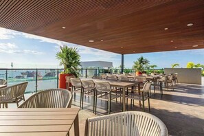 Eine Terrasse im Freien mit Tischen, Stühlen, Blumentöpfen und Blick auf den Ozean.