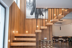 En trappe i træ med et moderne design, et spiseområde med borde og stole, og et bybillede som maleri på væggen.