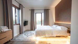 A modern bedroom with a bed, a flat-screen TV, a wooden dresser, and a large window.