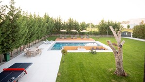 A backyard with a swimming pool, lounge chairs, and a ping pong table.