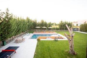 A backyard with a swimming pool, lounge chairs, and a ping pong table.