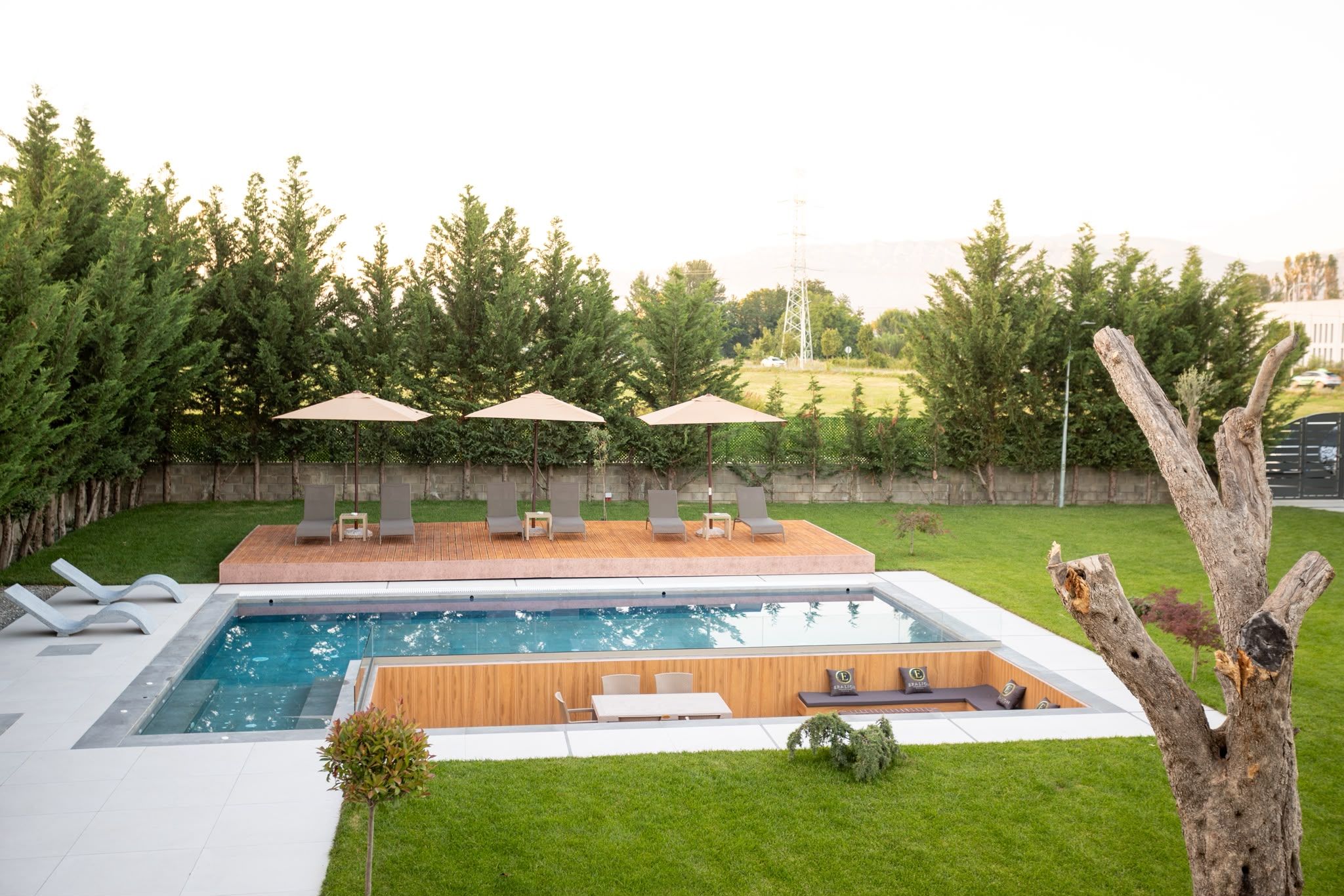 Een zwembad in de open lucht met een houten terras, ligbedden en parasols.