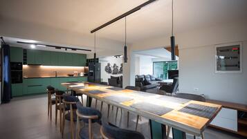 A modern kitchen with green cabinets, a wooden dining table with chairs, and a large window.