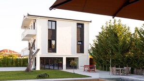 A modern two-story house with a swimming pool, outdoor furniture, and a tree in the yard.