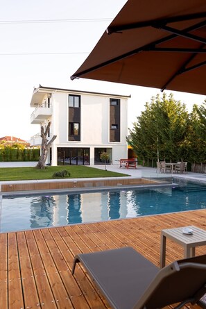 A modern two-story house with a swimming pool, outdoor furniture, and a tree in the yard.