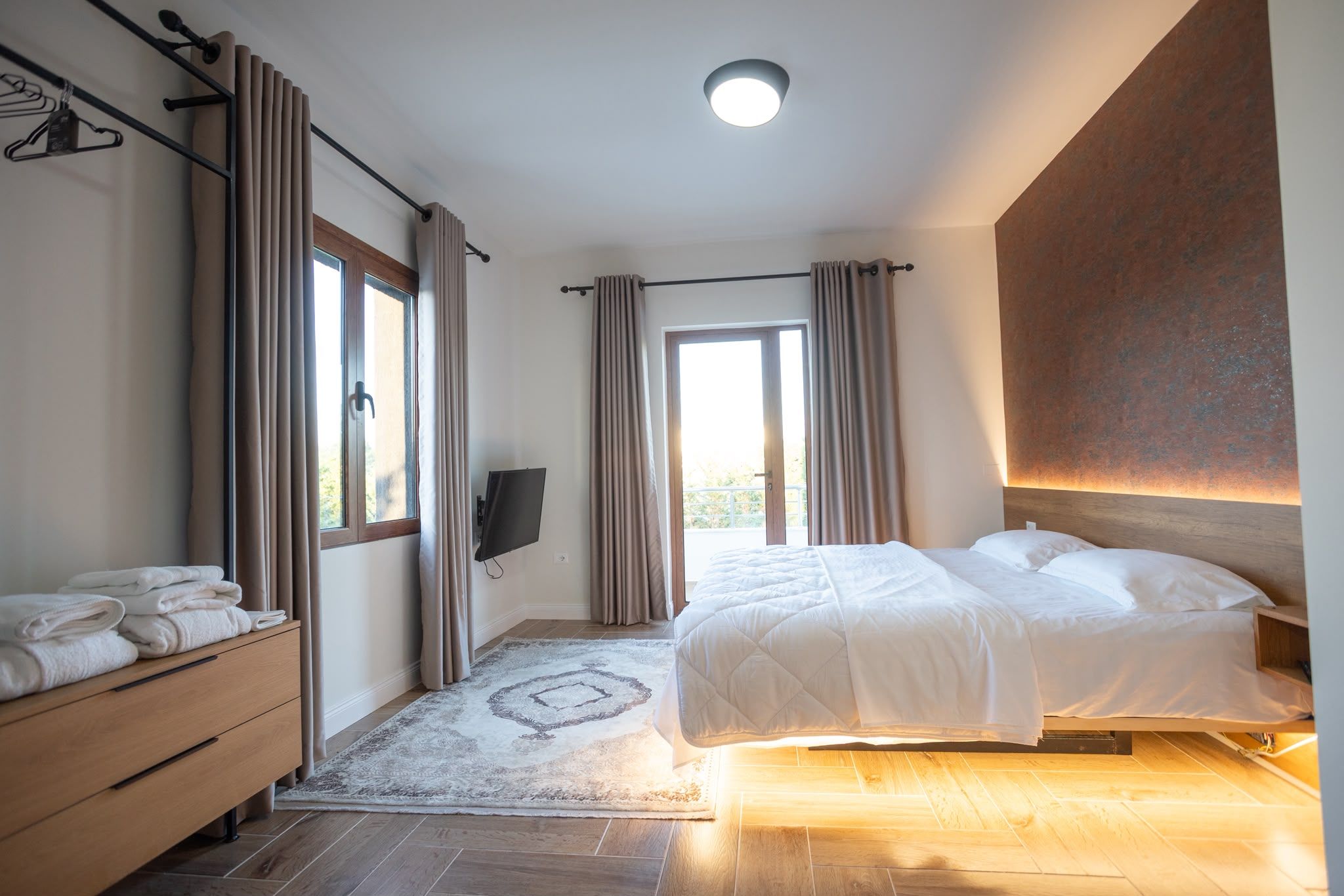 A bedroom with a bed, a wooden dresser, a TV, and a window with curtains.
