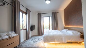 A bedroom with a bed, a wooden dresser, a TV, and a window with curtains.